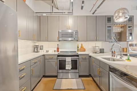 Modern kitchen with gray cabinets, gold hardware, and marble countertops.