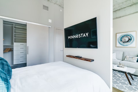 Modern bedroom with a large TV, a neatly made bed, and a stylish seating area.