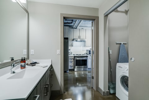 A modern bathroom with a view of a contemporary kitchen and laundry area.