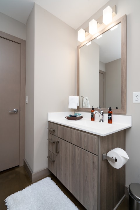 A modern bathroom with a wooden vanity, white countertop, and stylish lighting.
