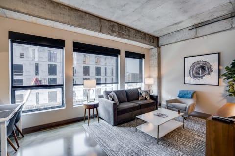 Modern living room with gray couch, armchair, and large windows.