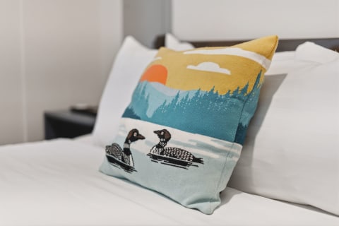 A colorful loon-patterned pillow on a nicely made bed, surrounded by bright white linens.