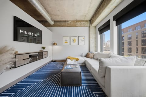 Modern urban living room with a grey sectional sofa, geometric rug, and large windows framing city views.