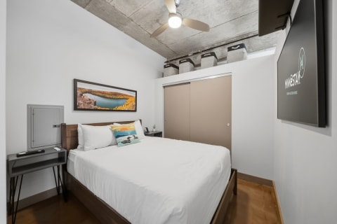 Modern urban bedroom with a cozy bed, concrete ceilings, and decorative photography.