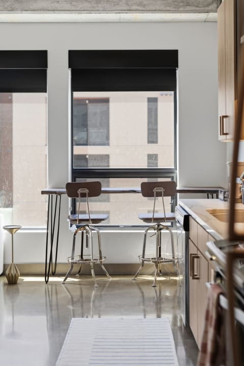 Bright and modern kitchen featuring a wooden bar table and contemporary stools by large windows.
