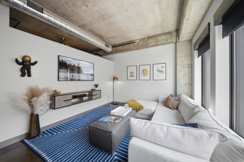 A stylish living room featuring a white sectional sofa, blue geometric rug, and industrial decor accents.
