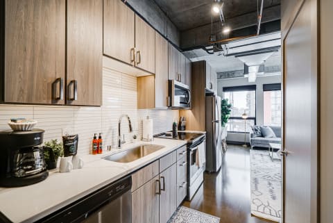 Modern kitchen with wood cabinets, stainless steel appliances, and a view of a living area.