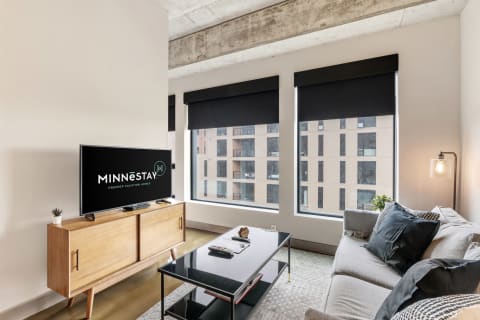 Modern living room with a TV, sofa, and large windows.