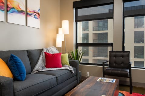 A modern living room with a gray sofa, colorful cushions, a black chair, and a wooden coffee table.