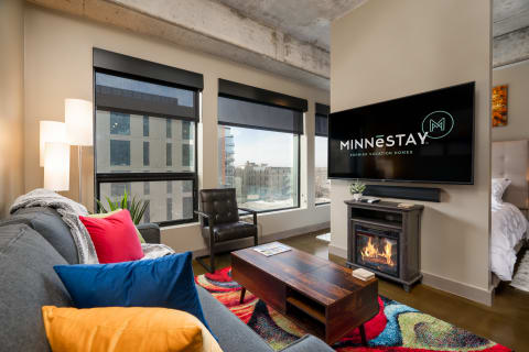 Modern living room with gray couch, colorful pillows, and a view through large windows.