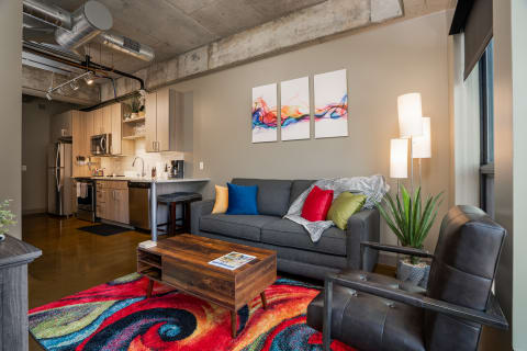 Living room featuring a colorful rug, modern sofa with throw pillows, and abstract wall art.