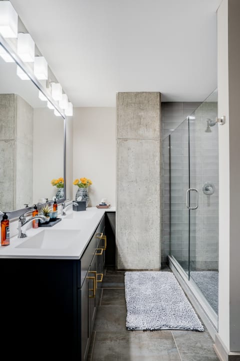 Modern bathroom featuring a dark vanity, concrete pillar, and walk-in shower.