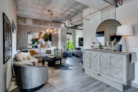 Modern living room with industrial features, featuring a gray sectional sofa, abstract art, and elegant lighting.