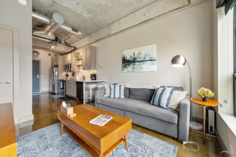 Stylish living room featuring a grey sofa, wooden coffee table, and modern kitchen.