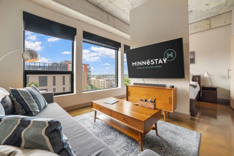 A modern living area with a gray sofa, wooden furniture, and a view of the city skyline.