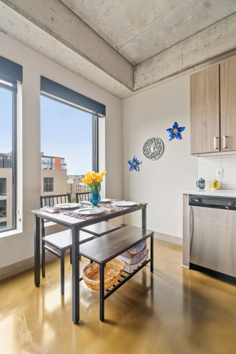 Modern dining area with black table, yellow tulips, and city view through large windows.