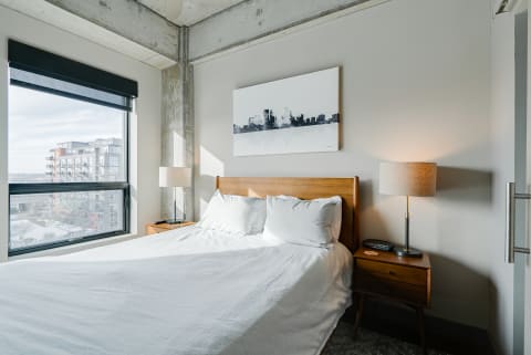 A modern bedroom with a wooden bed, white bedding, and large window allowing natural light.