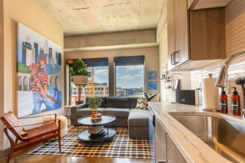 A stylish living area with a large artwork, grey sofa, and urban view.