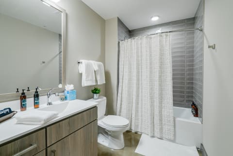 Modern bathroom with white countertop, amber soaps, and gray tiled shower.