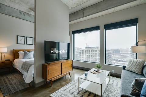 Modern apartment interior with a living space and bedroom area, large windows, and stylish furniture.
