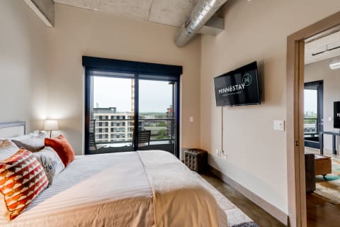 A modern bedroom featuring a bed, large window, and a television.