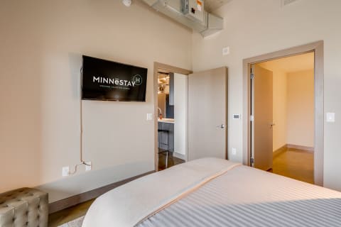 Modern bedroom with a neatly made bed and wall-mounted television.