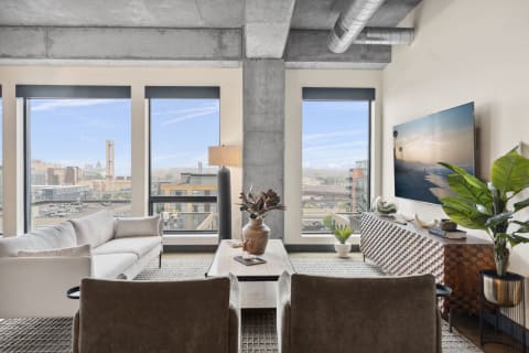 Modern living room with a sofa, chairs, and large windows showing a cityscape.