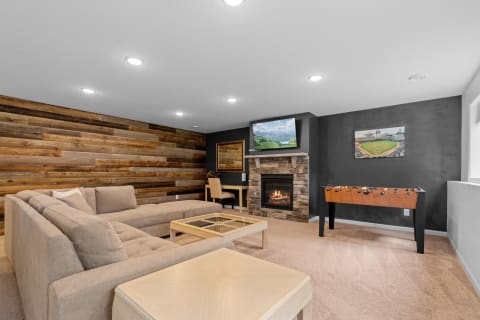 A modern living room featuring a sectional sofa, a stone fireplace, and a foosball table.