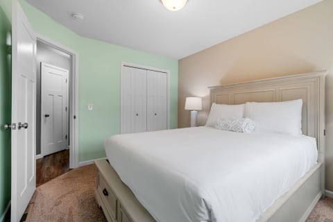 Cozy bedroom featuring a white bed with fluffy pillows and a mint green wall.