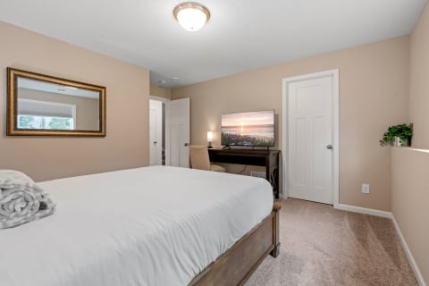 A cozy bedroom with a made bed, a mirror, a television, and a desk.