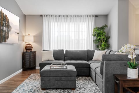 Cozy living room with gray sectional sofa, potted plant, and serene artwork on the wall.