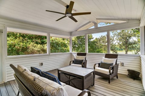 Screened porch with wicker chairs and coffee table overlooking a garden.
