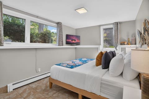 A cozy bedroom featuring large windows, a neatly made bed with colorful pillows, and decorative elements creating a peaceful ambiance.