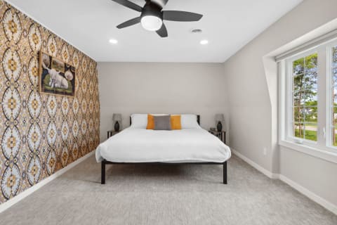 Modern bedroom with a large bed, decorative pillows, patterned wallpaper, and natural light from a window.