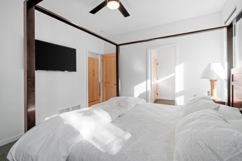 Modern bedroom with a white quilted bed, flat-screen TV, and elegant lamp.