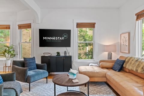 Stylish living room with tan leather sofa, gray chair, and green plants.