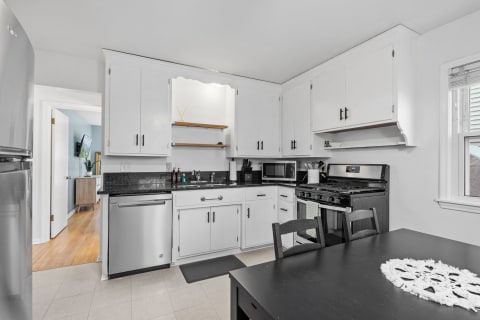 A minimalist kitchen featuring white cabinets, black countertops, and stainless-steel appliances.