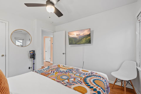 Cozy bedroom with a patterned quilt, TV, and white furniture.