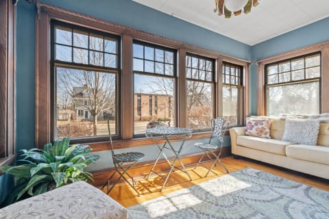 Cozy sunroom with large windows, a table and chairs, and a sofa with pillows.