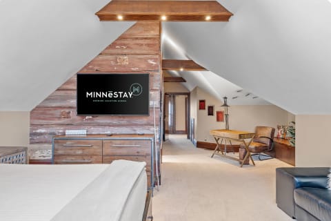 A well-designed attic space with a bed, TV, and workspace featuring rustic decor.