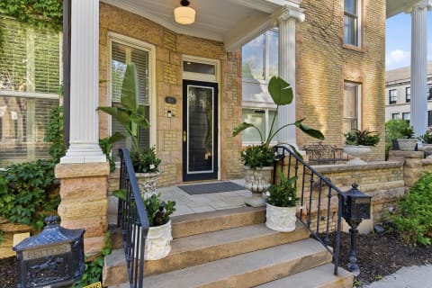 An inviting front entrance featuring brick construction, white columns, and lush planters in a peaceful neighborhood.