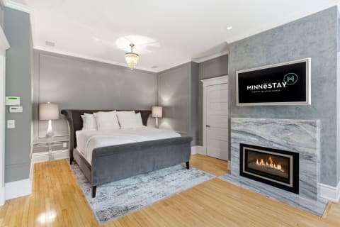An elegant bedroom with plush bed, stylish lighting, and a modern fireplace.