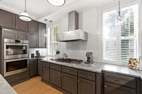 Contemporary kitchen featuring dark cabinets, marble countertops, and stainless steel appliances with natural light.