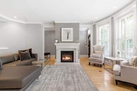 A stylish living room featuring a brown sectional sofa, gray armchairs, a fireplace, and a soft rug on wooden flooring.