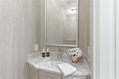 A stylish bathroom featuring a marble countertop with toiletries, a mirror, and decorative flowers, creating a serene atmosphere.