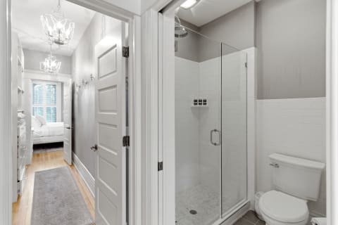 Spacious bathroom featuring a walk-in shower with white tiles and a cozy hallway leading to a bedroom.