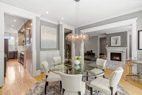 A stylish dining area with a glass table, plush chairs, and a cozy fireplace in the background.