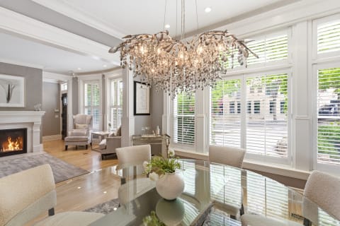 A beautifully designed dining room with a glass table, crystal chandelier, and a cozy fireplace.