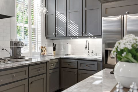 A stylish kitchen featuring gray cabinets, marble countertops, and stainless steel appliances, illuminated by natural light.
