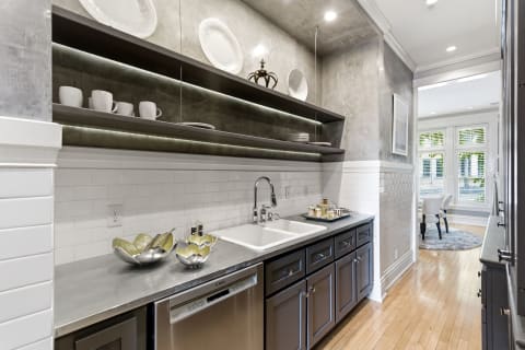 A modern kitchenette with gray cabinetry, white subway tiles, and open shelves displaying dinnerware.
